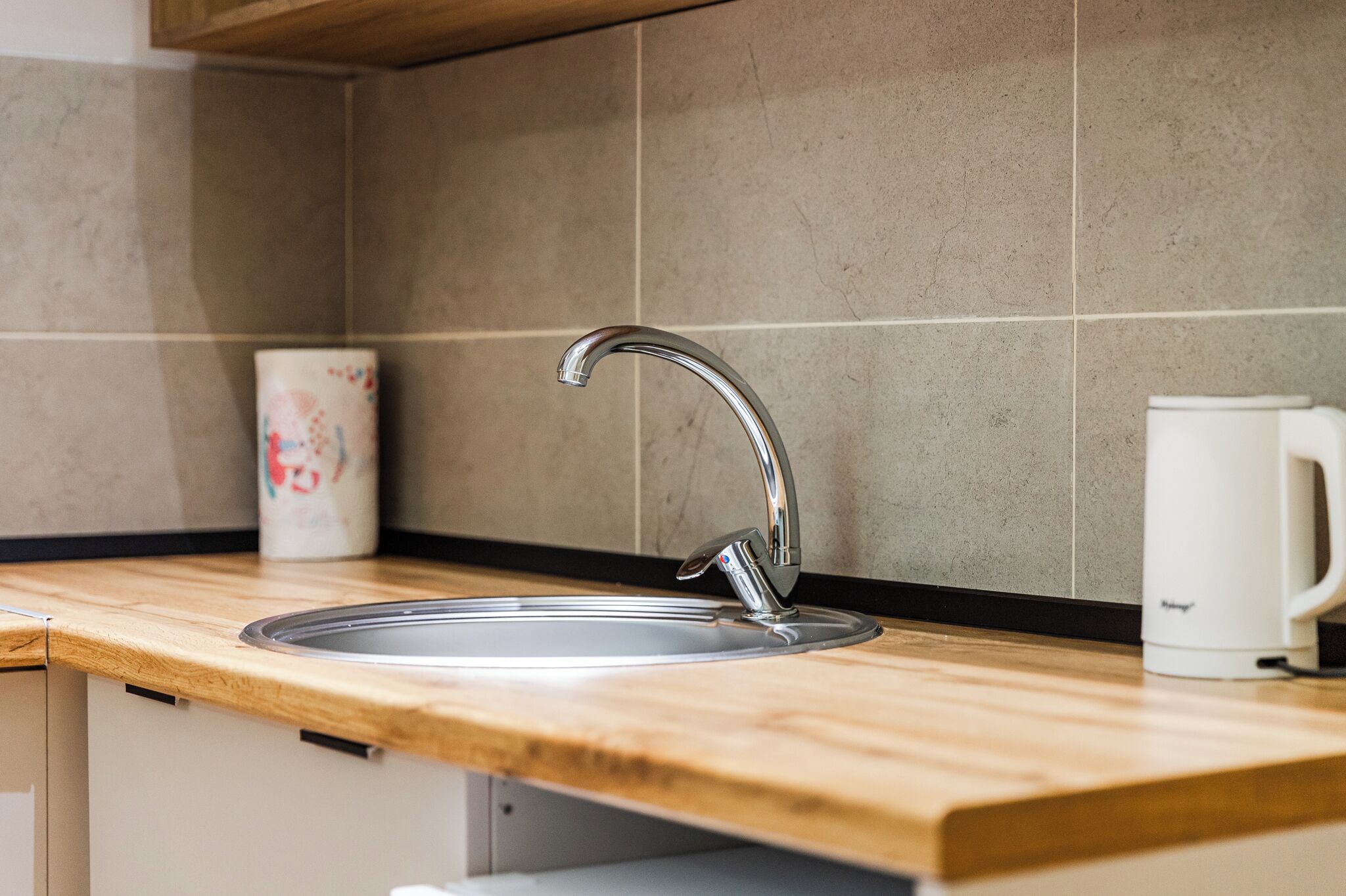 A kitchen with a stainless steel sink, a wooden countertop, and a white mug.