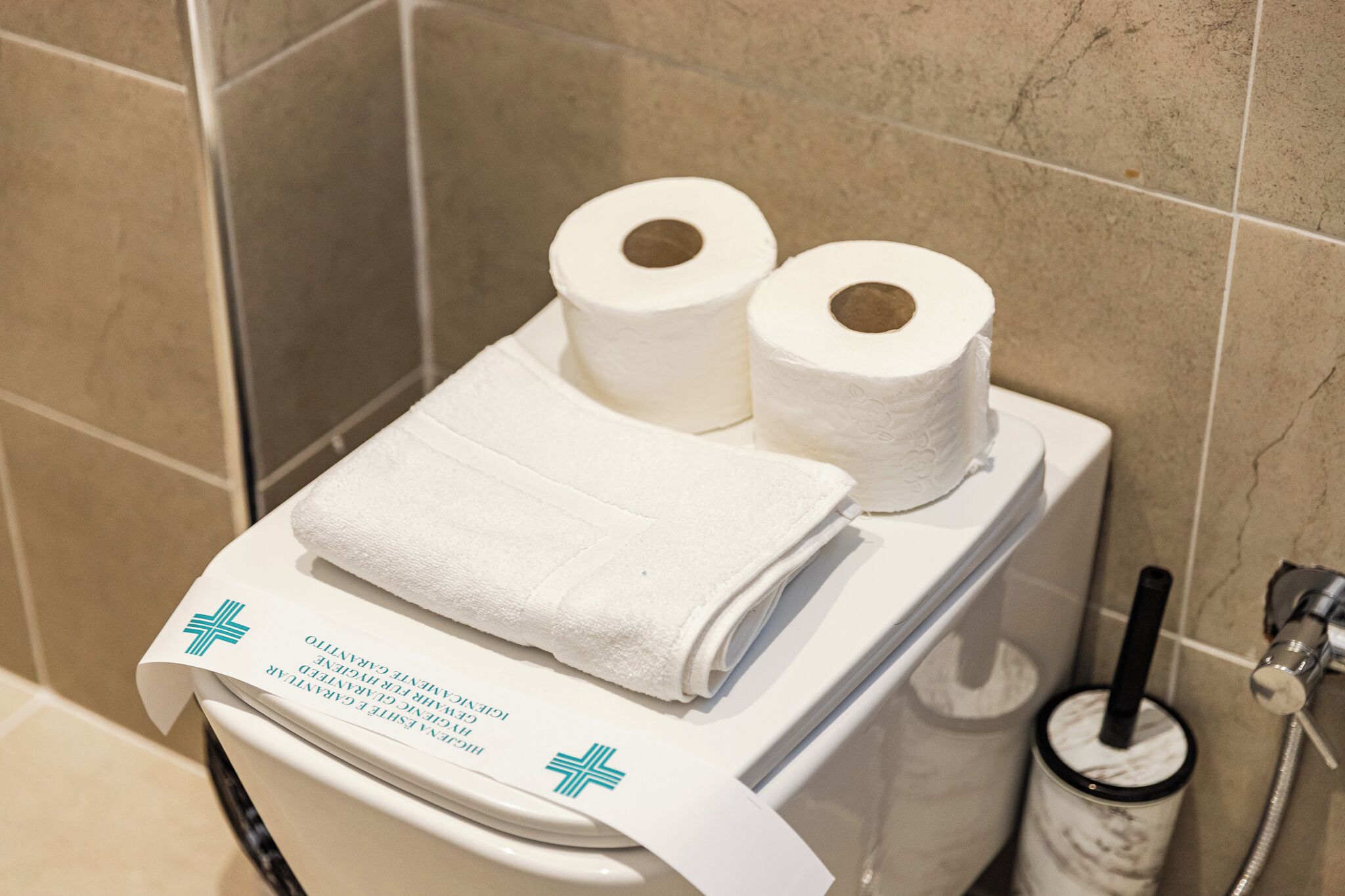 Une salle de bain avec deux rouleaux de papier toilette, une serviette blanche pliée et un distributeur de serviettes en papier.