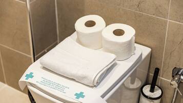 Une salle de bain avec deux rouleaux de papier toilette, une serviette blanche pliée et un distributeur de serviettes en papier.