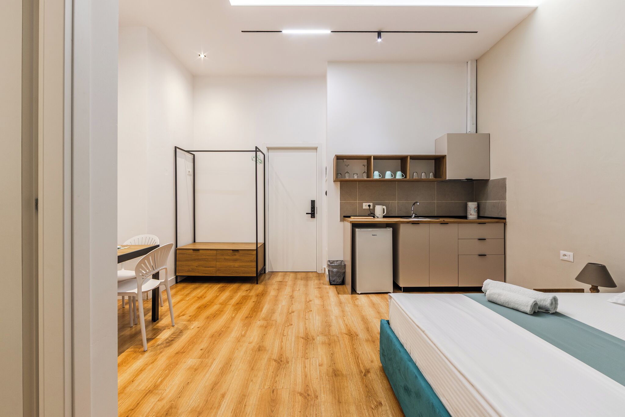 A compact hotel room with a bed, a small kitchenette, a dining area with a table and chairs, and a separate bathroom with a shower.