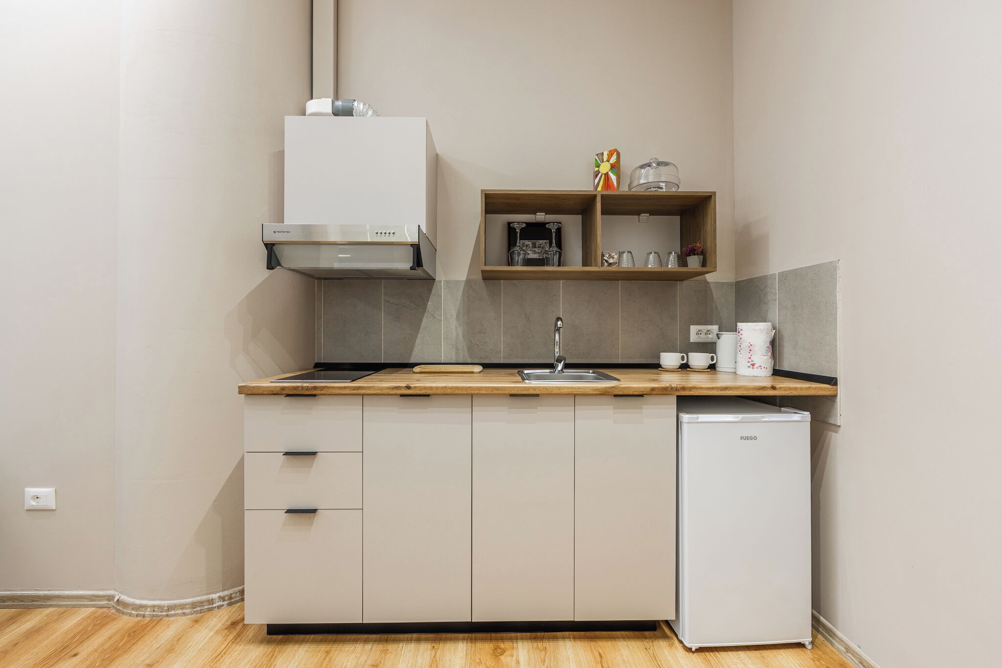 A compact kitchen with a built-in dishwasher, a stainless steel range hood, and a wooden countertop.