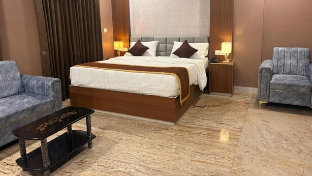 A hotel room with a large bed, two bedside tables, a sofa, and a coffee table. - Raj Hussain Landmark Hotel (Mayiladuthurai)