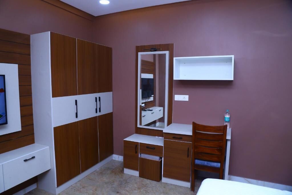 A bedroom with a bed, a wooden wardrobe, a mirror, a desk, and a shelf.
