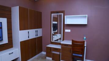 A bedroom with a bed, a wooden wardrobe, a mirror, a desk, and a shelf.