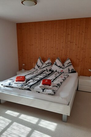 Un lit avec une couvre-lit à motifs et des oreillers, une table de chevet et un mur en bois.