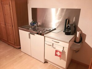 A compact kitchenette with a stainless steel stove, a coffee machine, and a small sink. - Ferienwohnungen Teuriblick A&B, (Splügen), by Interhome (Splügen)
