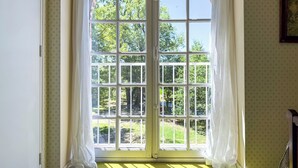 Ein Zimmer mit einem großen Bogenfenster, Vorhängen und einem gemusterten Wandteppich.