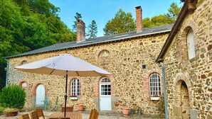 Ein Gebäude aus Stein mit Kiesterrasse, Sitzgelegenheiten im Freien und einem großen Sonnenschirm.