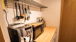 A compact kitchenette with a coffee machine, microwave, and hanging utensils. - Ferienwohnungen Felder, (Splügen), by Interhome (Splügen)