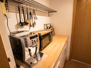 A compact kitchenette with a coffee machine, microwave, and hanging utensils. - Ferienwohnungen Felder, (Splügen), by Interhome (Splügen)