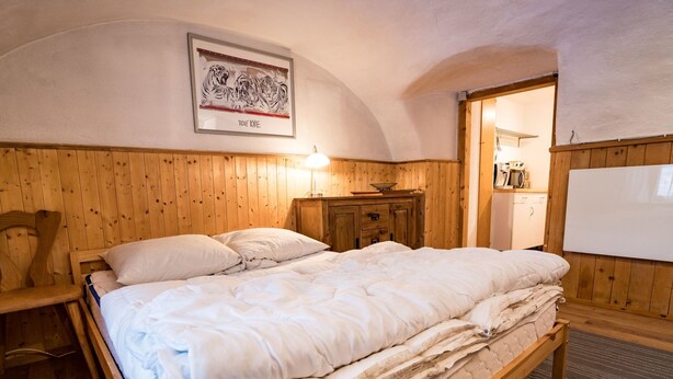 A wooden-framed bed with white bedding, a wooden headboard, a nightstand, a wooden cabinet, a framed picture on the wall, and a whiteboard. - Ferienwohnungen Felder, (Splügen), by Interhome (Splügen)