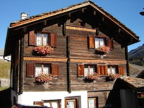 A traditional wooden chalet with multiple windows, some with shutters, and flower boxes on the windowsills. - Ferienwohnungen Felder, (Splügen), by Interhome (Splügen)