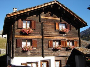 A traditional wooden chalet with multiple windows, flower boxes, and a clear sky in the background. - Ferienwohnungen Felder, (Splügen), by Interhome (Splügen)