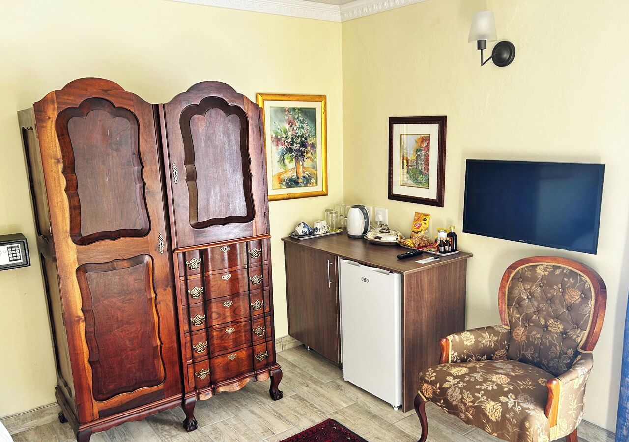 A room with a wooden cabinet, a white refrigerator, a floral armchair, a television, and a painting on the wall.