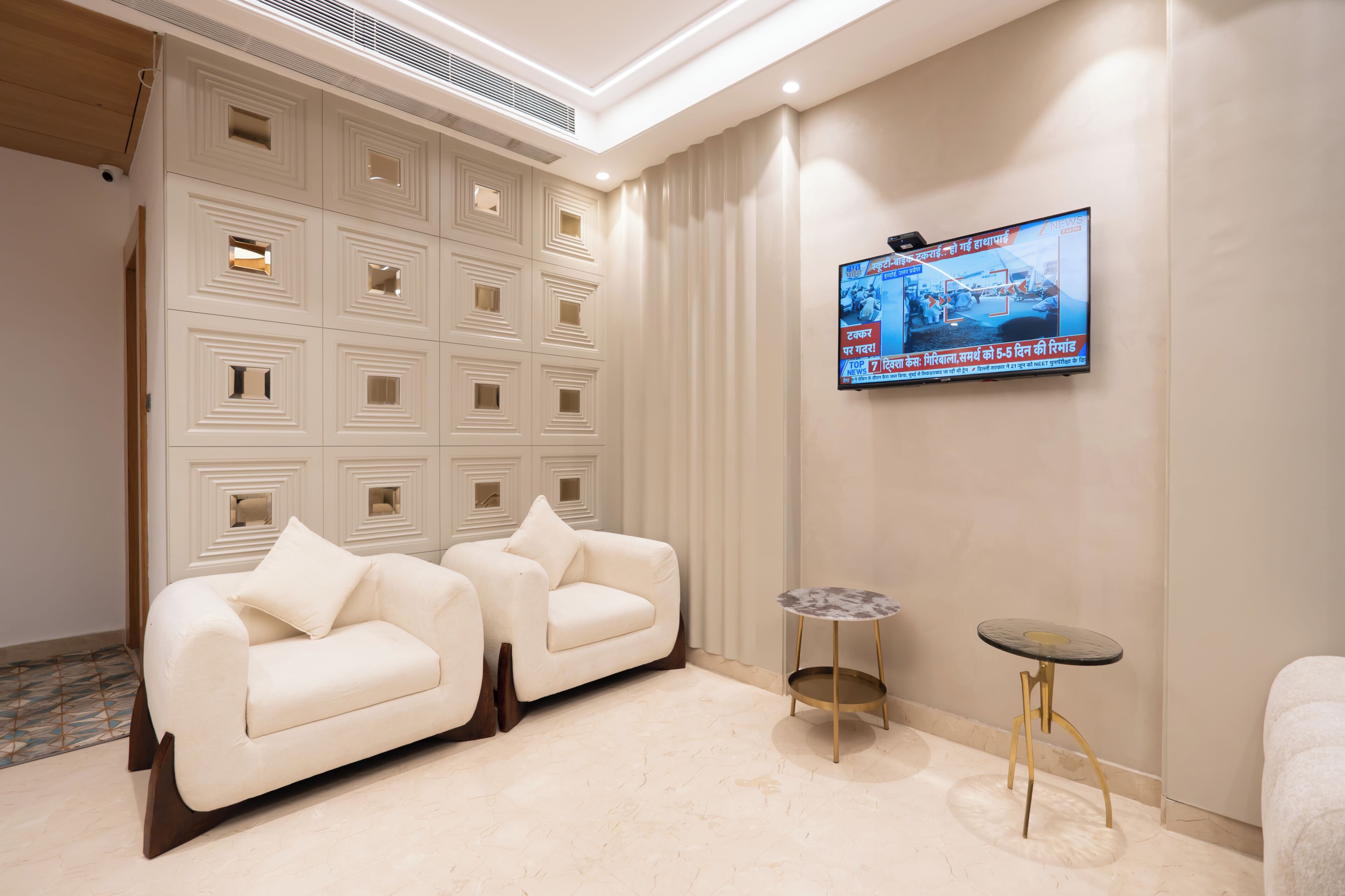 A modern hotel room with a beige sofa, a small round table, and a TV mounted on the wall.