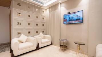 A modern hotel room with a beige sofa, a small round table, and a TV mounted on the wall.