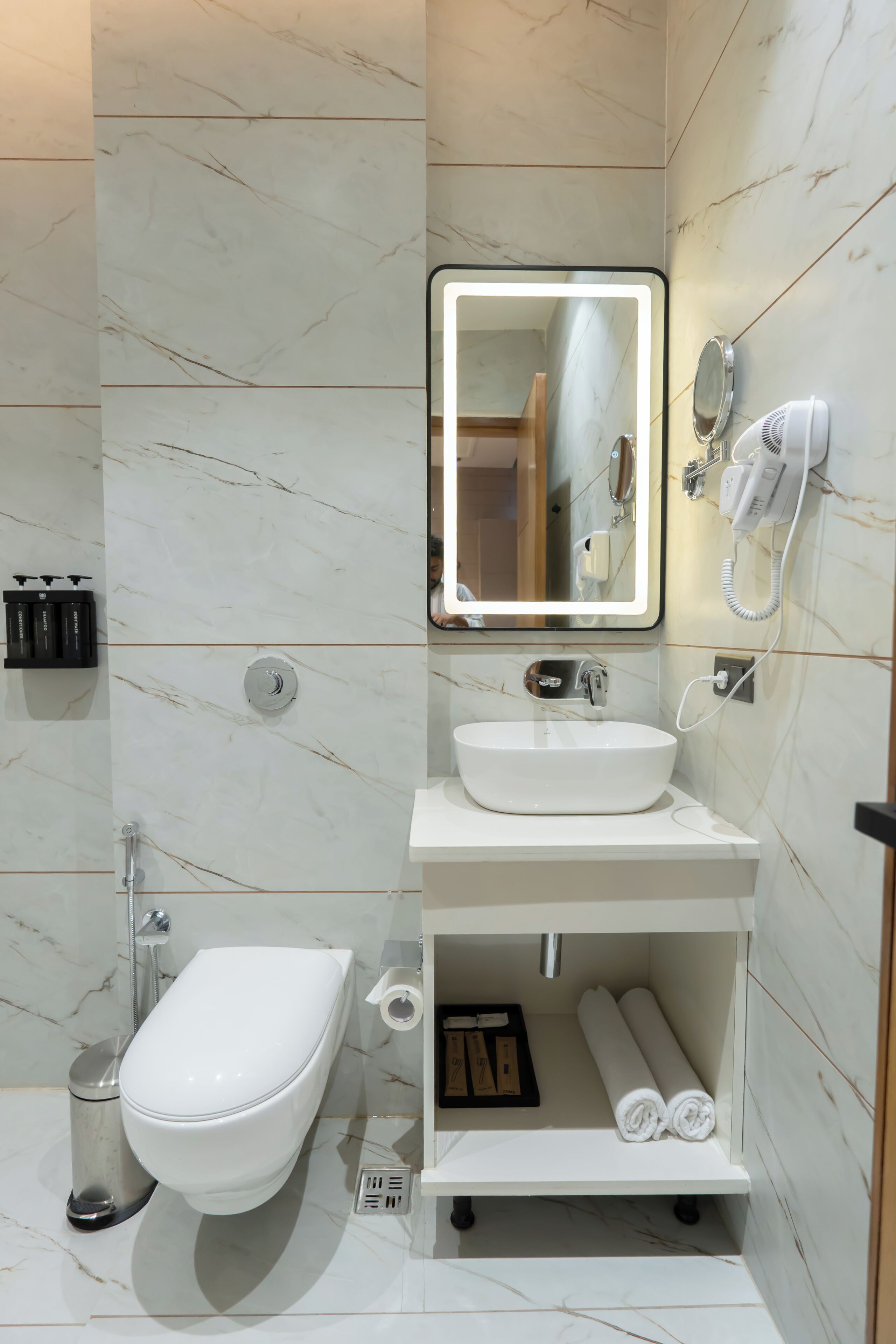 A modern bathroom with a toilet, sink, mirror, and hairdryer.