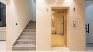 A modern elevator with a metallic interior, adjacent to a staircase with a handrail and carpeted steps. - Amara Portico (Amritsar)
