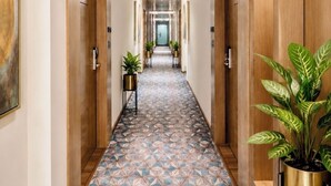 A hotel hallway with a geometric patterned floor, wooden doors, and potted plants. - Amara Portico (Amritsar)