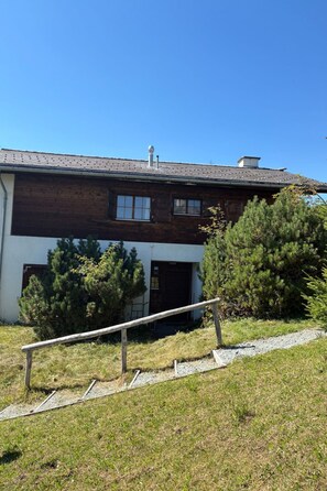 A two-story wooden building with a sloped roof, a visible chimney, and a small porch area.