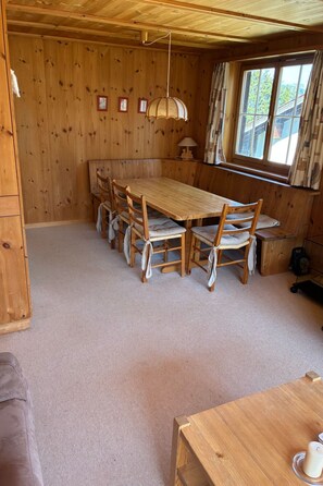 Interior em madeira com uma grande mesa de jantar e cadeiras, um abajur e uma janela com cortinas.