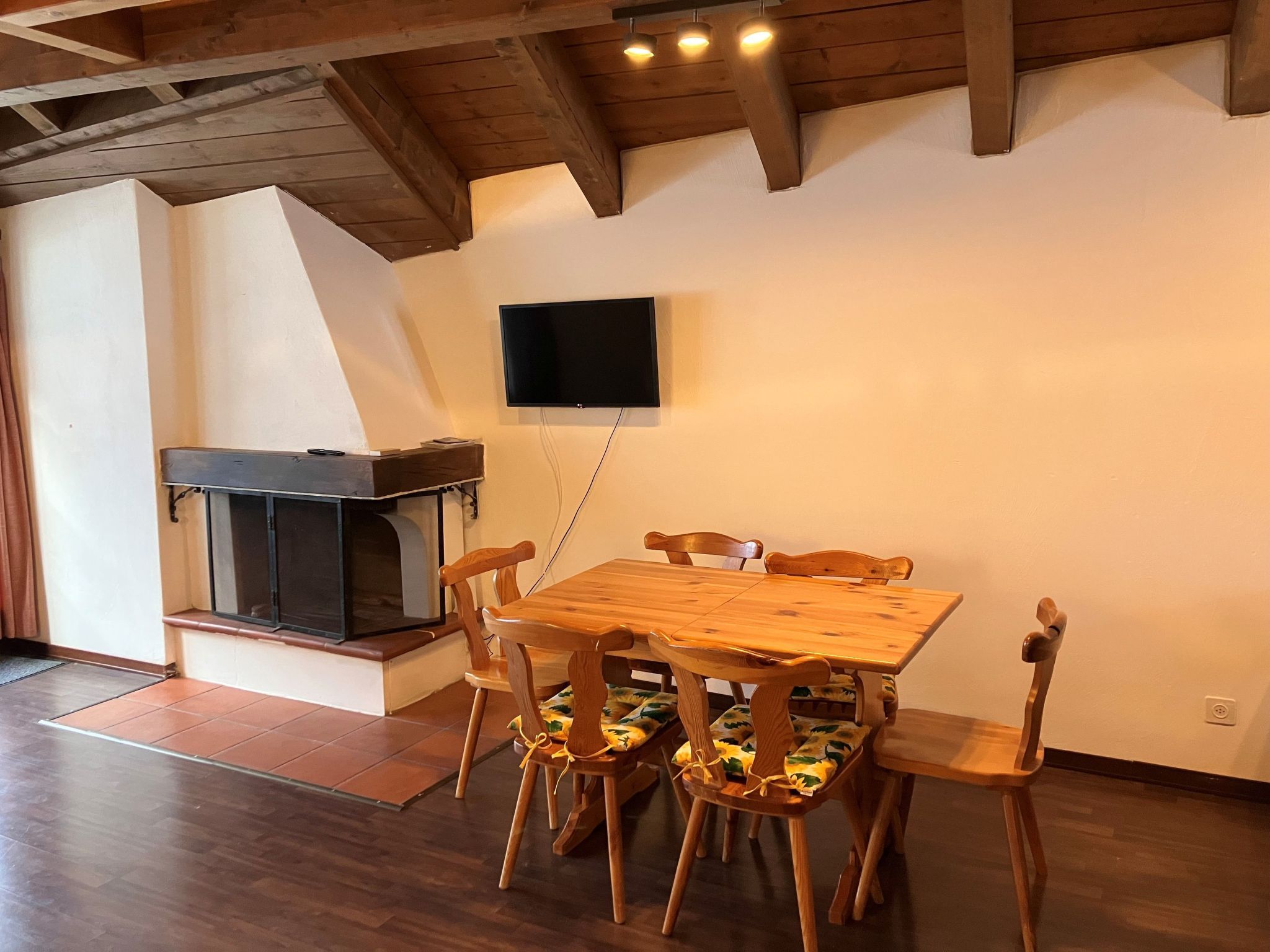 Un coin repas avec une table et des chaises en bois, un téléviseur fixé au mur et une cheminée.
