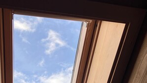 Un tragaluz en una habitación con vigas de madera y vista al cielo despejado.