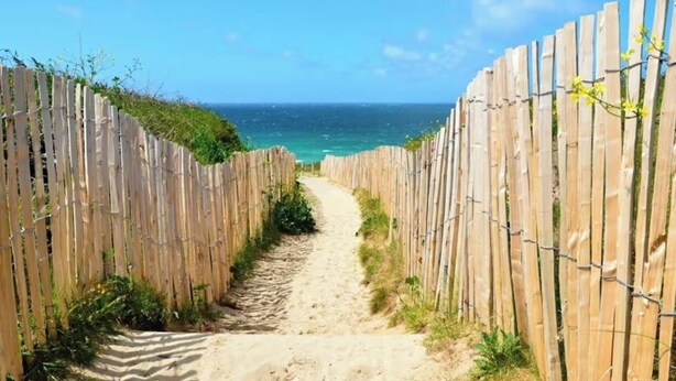 Un camí de sorra flanquejat per tarrassos de fusta que condueix a una platja.