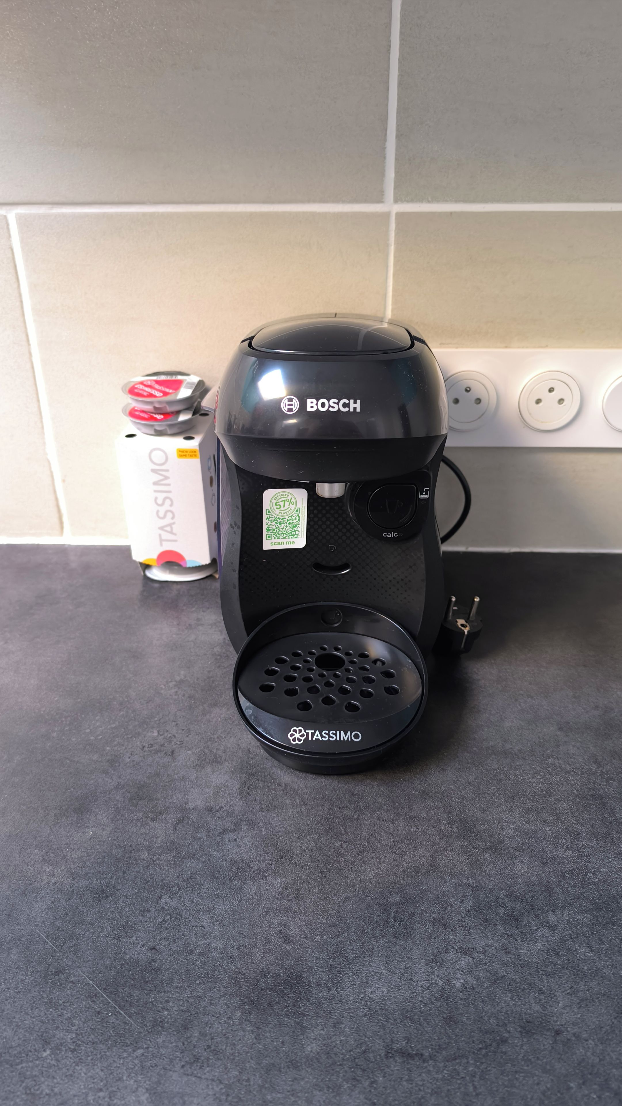 Eine Kaffeemaschine steht auf einer Küchenarbeitsplatte, in der Nähe befindet sich eine Tassimo-Kapselbox.