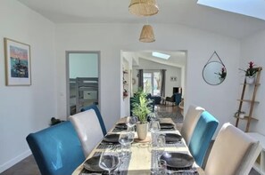 A dining area with a table set for four, chairs, hanging wicker lamps, and a view into another room. - Chic House with Hot Tub—Near the Beaches of Locmaria (Locmaria-Plouzané)