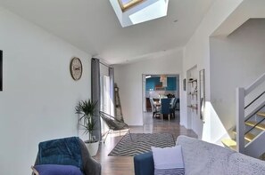 A modern living room with a sofa, a chair, a plant, and a dining area in the background. - Chic House with Hot Tub—Near the Beaches of Locmaria (Locmaria-Plouzané)