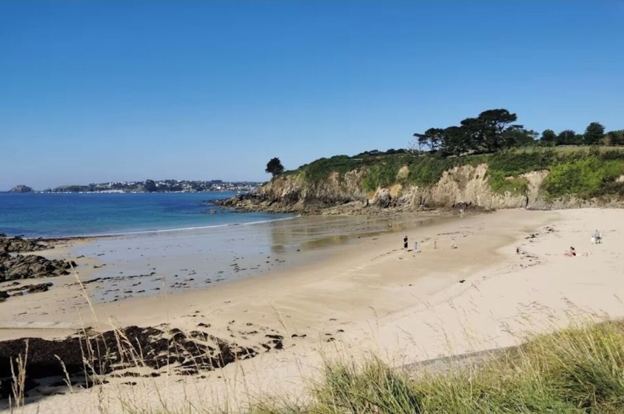 A beach with a clear sky, rocky shoreline, and sparse vegetation.