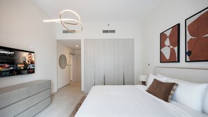 Moderni hotellihuone, jossa on suuri sänky, seinälle asennettu televisio ja taideteoksia sängyn yläpuolella.