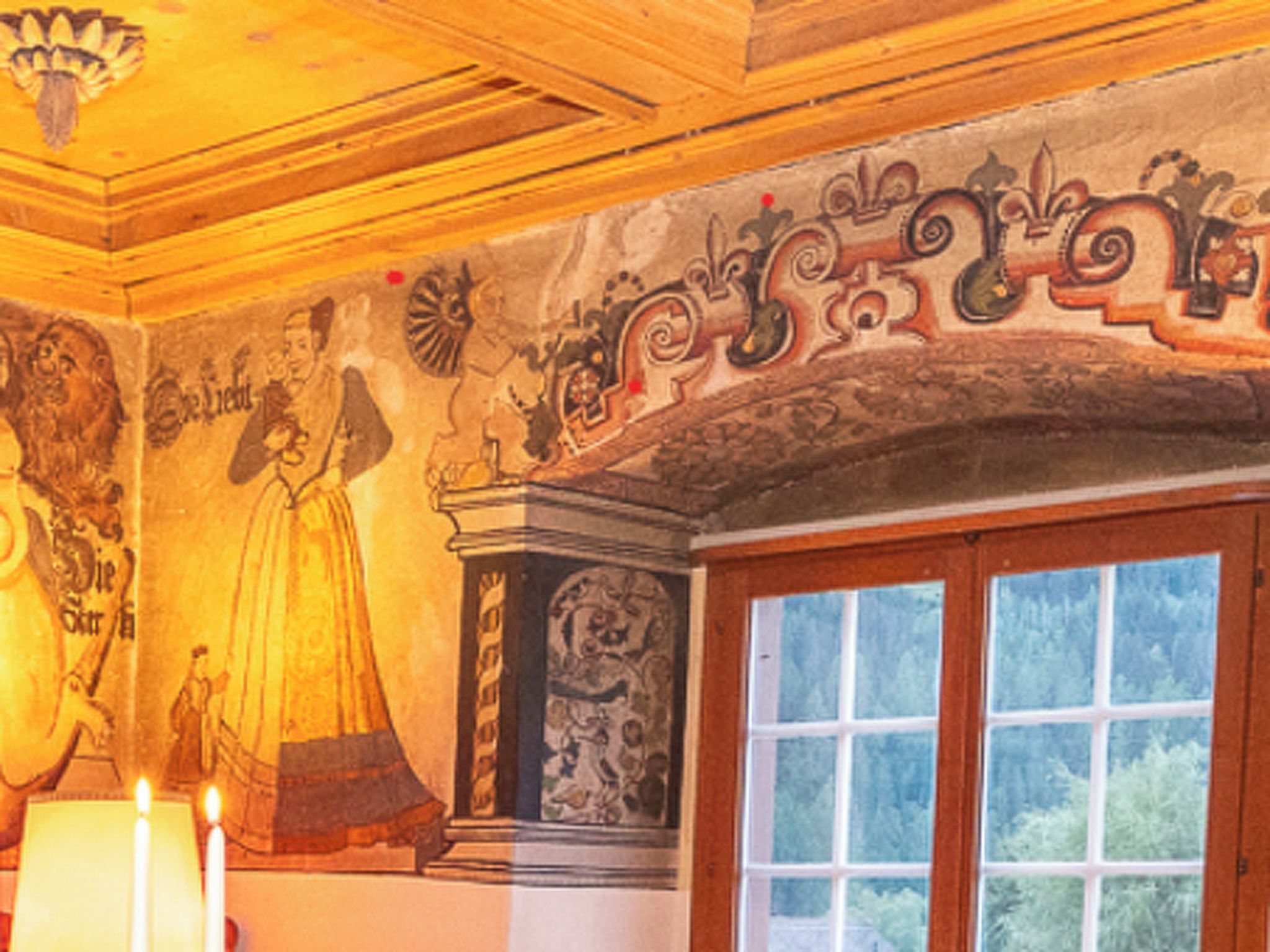 A room with a large mural, a window, and a candle on a table.