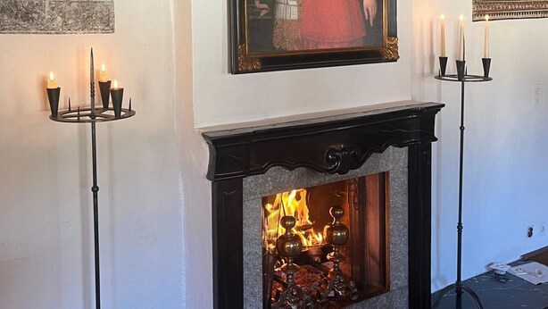 Una chimenea con un retrato encima, un candelabro a la izquierda y un tapiz a la derecha.