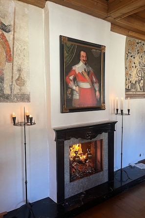 Una chimenea con un retrato sobre ella, un candelabro a cada lado y un tapiz en la pared.