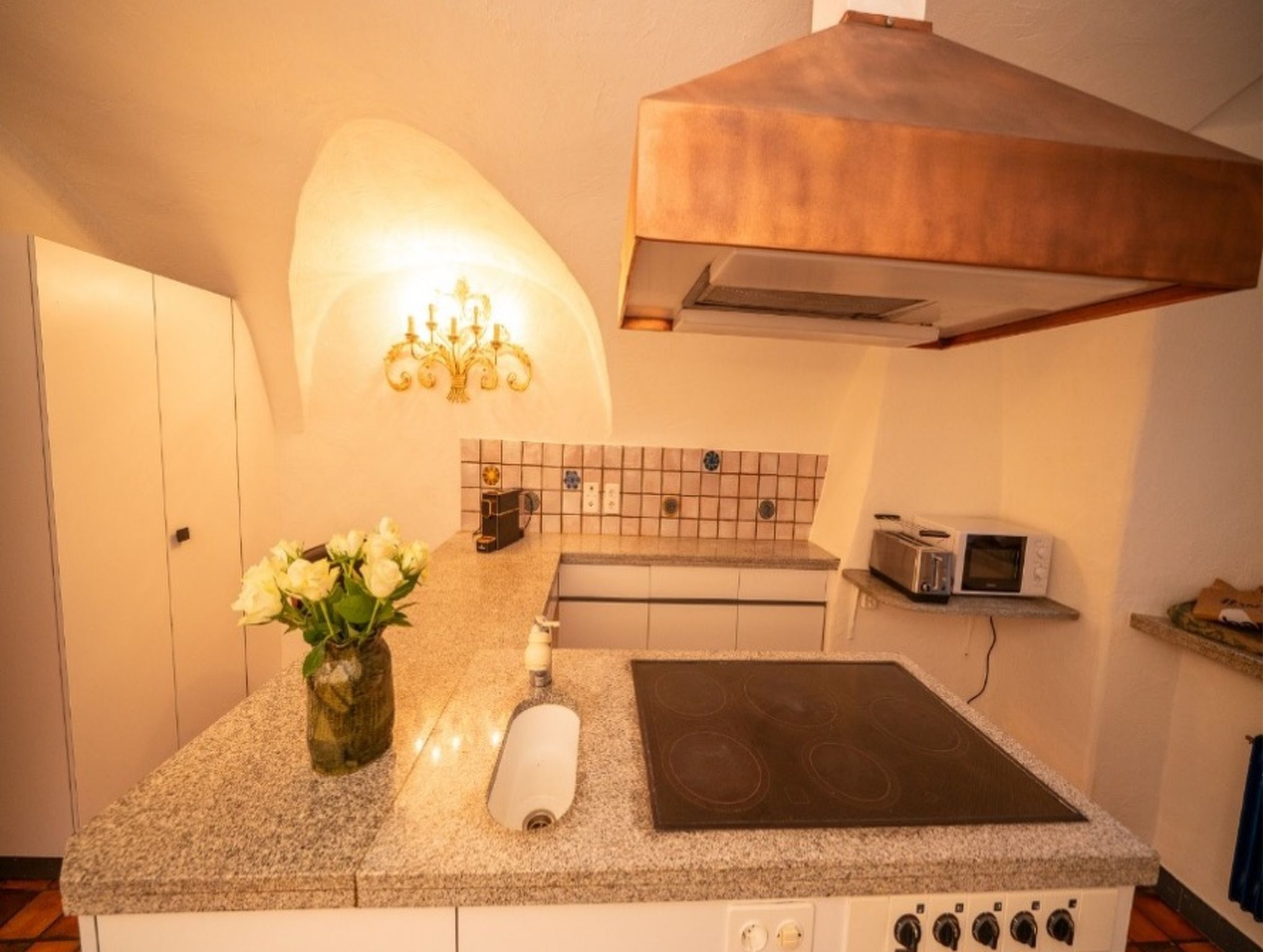 Una cucina con un piano di lavoro in granito, un tostapane in acciaio inossidabile, un forno a microonde, un fornello e un vaso con fiori bianchi.