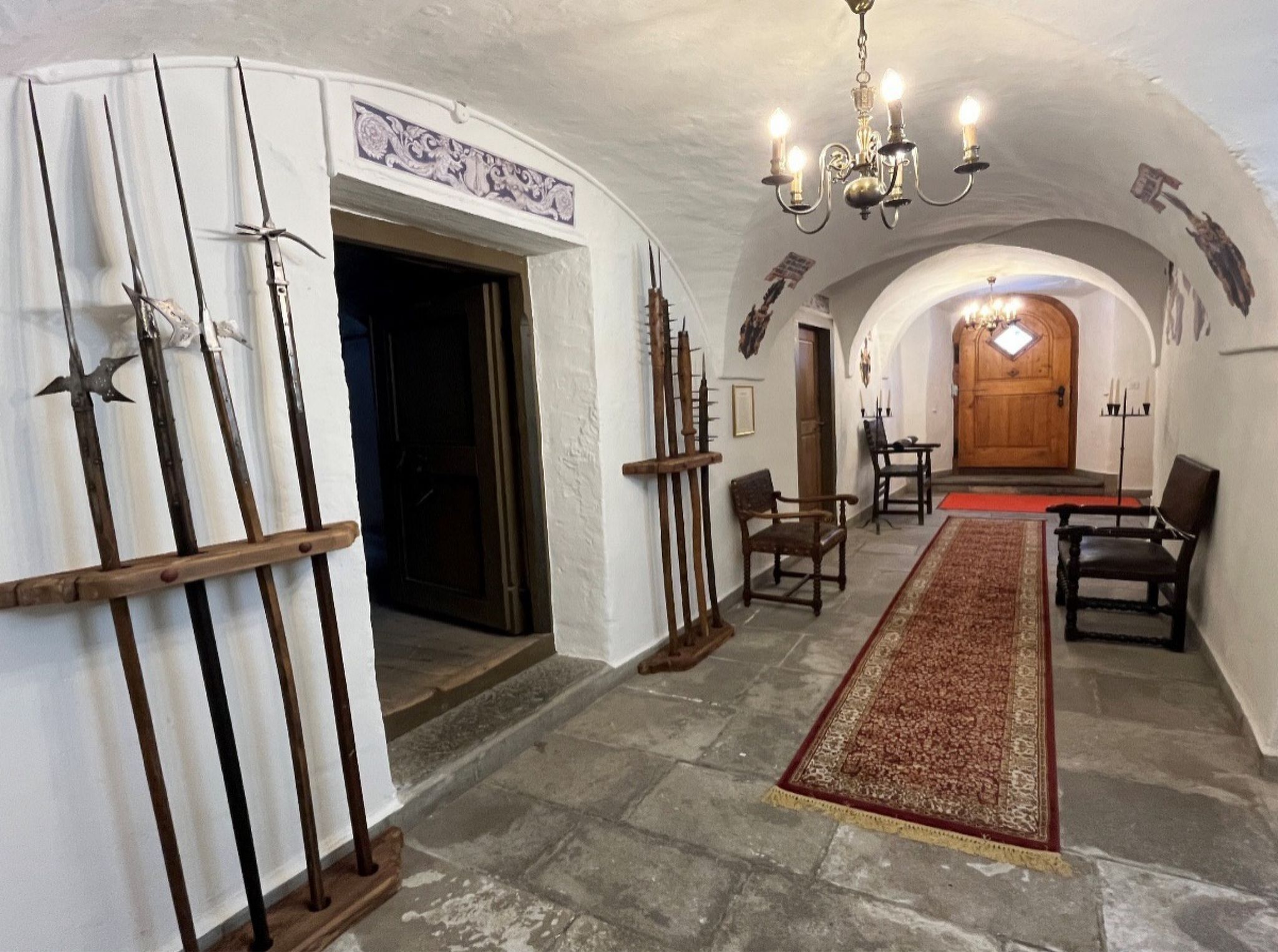 Un corridoio con una porta in legno, un lampadario e un tappeto decorato.