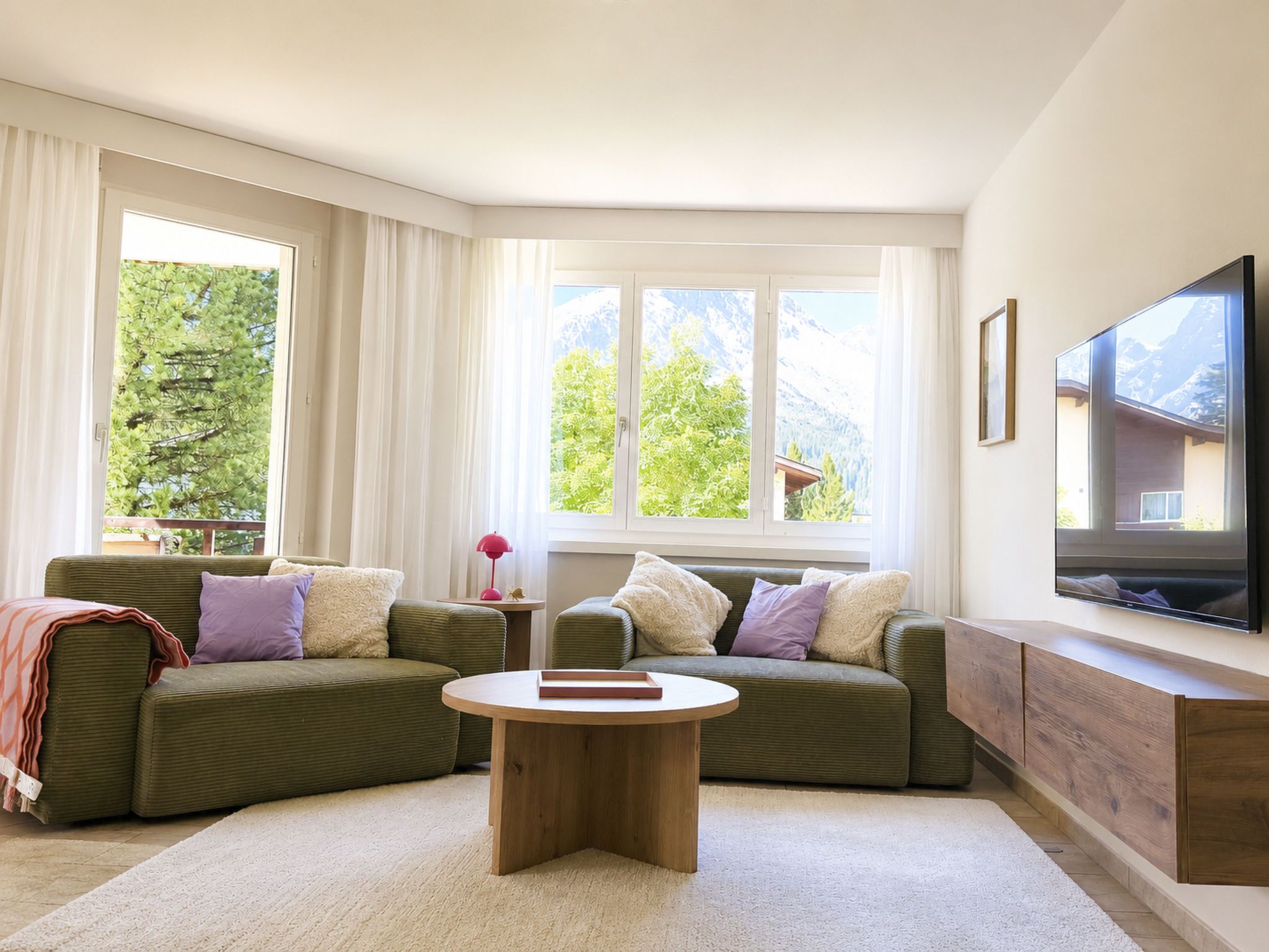 A modern living room with a green sofa set, a coffee table, and a flat-screen TV mounted on the wall.