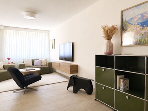 A modern living room with a sofa, a black gaming chair, a coffee table, a flat-screen TV, a bookshelf, and a painting on the wall. - Montefiori Jama Stay Appartement/Fewo, Toilette und Bad/Dusche getrennt, 6-Bettw by Interhome (Arosa)