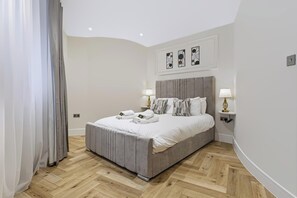 A modern bedroom with a large bed, two bedside lamps, and a herringbone wooden floor. - Perched above Matlock Bath, 37 Steps is a stylish upside-down home designed to make the most of its incredible views across the valley. With a sociable open-plan living space, four ensuite bedrooms, and a showstopping terrace with hot tub. (Matlock Bath)