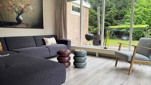 Una sala de estar moderna con un sofá gris, una silla de madera y un ventanal grande.