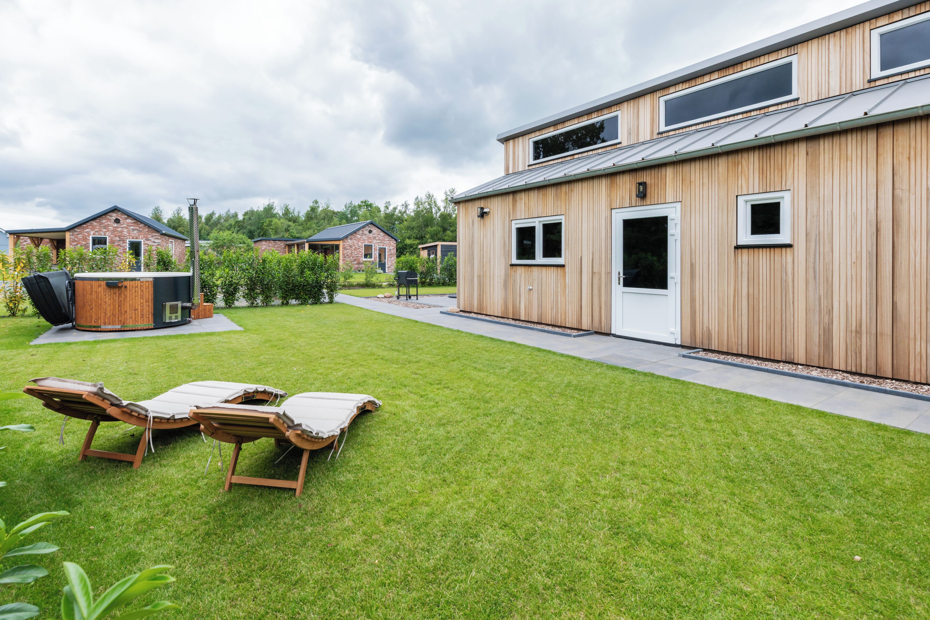 A modern building with a wooden exterior, a grassy lawn, and two lounge chairs.
