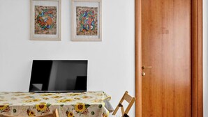 Un comedor con una mesa cubierta por un mantel floral, dos cuadros en la pared y una puerta de madera.