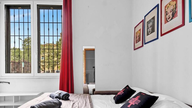 Un dormitorio con una cama, una ventana con rejas y cuadros en la pared.