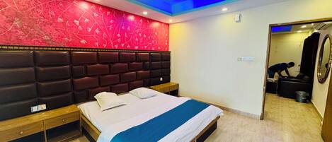 A hotel room with a bed, a headboard, a ceiling fan, a red patterned wall, and a door leading to a bathroom.