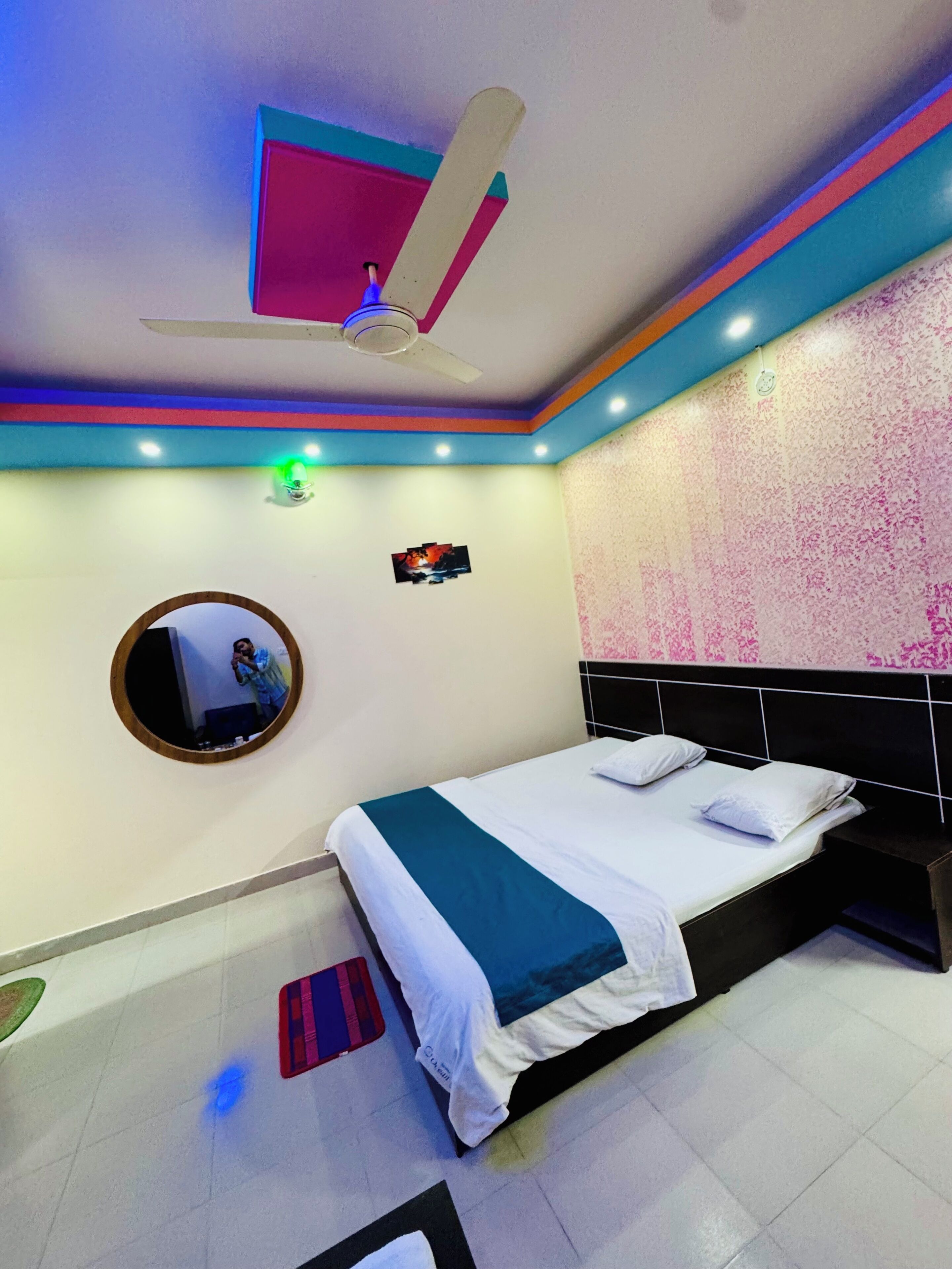 Une chambre à coucher avec un lit, un ventilateur de plafond, un miroir et un téléviseur fixé au mur.