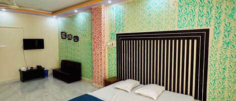 Un dormitorio con cama, ventilador de techo, televisor y pared con diseño.