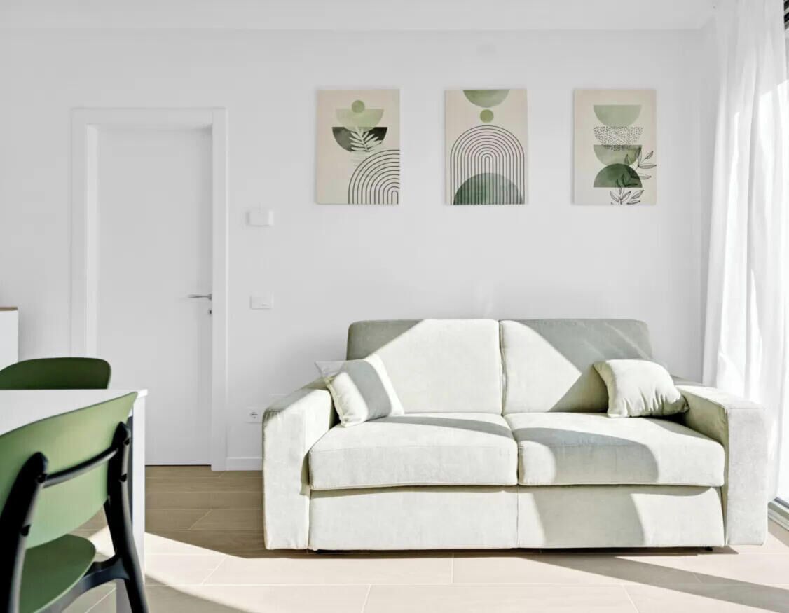 Un soggiorno moderno con un divano bianco, un tavolo da pranzo con sedie e arte astratta alle pareti.