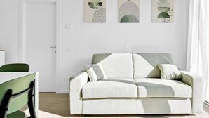 Una sala de estar moderna con un sofá blanco, una mesa de comedor con sillas y arte abstracto en la pared.